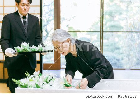 An elderly woman performing a flower vase ceremony at a funeral coffin ceremony An elderly woman performing a flower vase ceremony at a funeral coffin ceremony 95368118