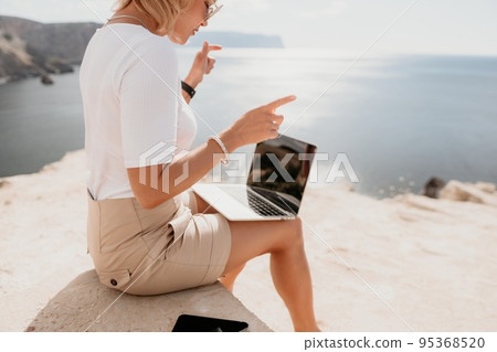 Digital nomad, Business woman working on laptop by the sea. Pretty lady typing on computer by the sea at sunset, makes a business transaction online from a distance. Freelance, remote work on vacation Digital nomad, Business woman working on laptop by the sea. Pretty lady typing on computer by the sea at sunset, makes a business transaction online from a distance. Freelance, remote work on vacation 95368520