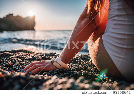 Young woman with long hair in white swimsuit and boho style braclets practicing outdoors on yoga mat by the sea on a sunset. Women's yoga fitness routine. Healthy lifestyle, harmony and meditation 95368641
