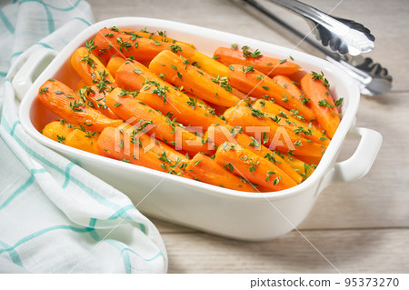Fried baby carrots with fresh thyme in a ceramic form on a wooden table. Caramelized Carrots. A healthy carrot dish that is rich of vitamin A. 95373270