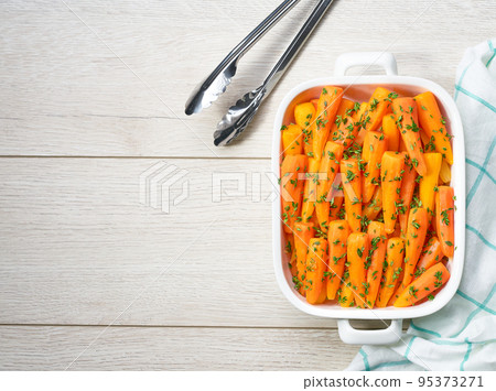 baked honey glazed baby carrots with thyme in a ceramic form on a wooden table,top view. baked honey glazed baby carrots with thyme in a ceramic form on a wooden table,top view. 95373271