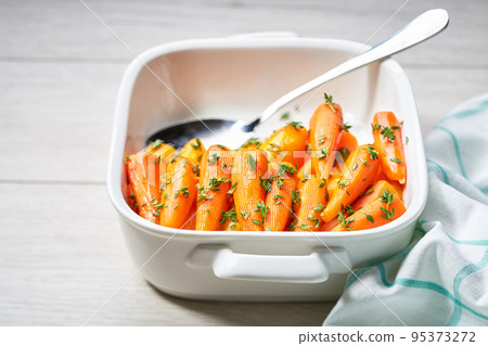 baked honey glazed baby carrots with thyme in a ceramic form on a wooden table, selective focus. baked honey glazed baby carrots with thyme in a ceramic form on a wooden table, selective focus. 95373272