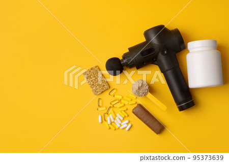 Therapeutic percussive massage gun, fit meal, pills, sport energy bar, protein on yellow background - concept of modern sport activity and diet, health lifestyle routine, wellness, healthcare Therapeutic percussive massage gun, fit meal, pills, sport energy bar, protein on yellow background - concept of modern sport activity and diet, health lifestyle routine, wellness, healthcare 95373639