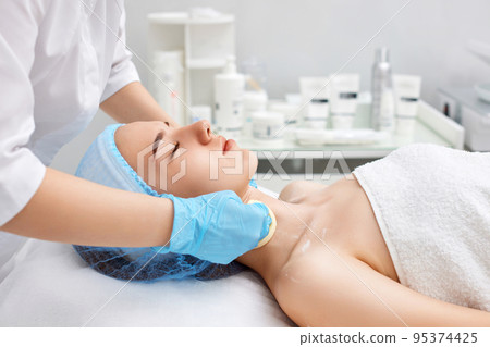 beautician cleanses skin of beautiful woman with a sponge. beautician cleanses skin of beautiful woman with a sponge. 95374425