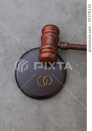 Law theme. Judge gavel wedding rings on concrete stone grey background. Divorce proceedings. Mallet of judge deciding on marriage divorce, marital agreement, legalities of divorce Law theme. Judge gavel wedding rings on concrete stone grey background. Divorce proceedings. Mallet of judge deciding on marriage divorce, marital agreement, legalities of divorce 95376138