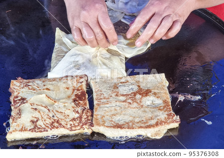 Person cooking murtabak on pan at street market during muslim iftar season Person cooking murtabak on pan at street market during muslim iftar season 95376308