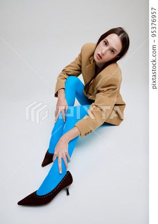 Portrait of young beautiful girl posing in blue tights, oversized jacket and heels isolated over grey studio background. Fashionable Portrait of young beautiful girl posing in blue tights, oversized jacket and heels isolated over grey studio background. Fashionable 95376957