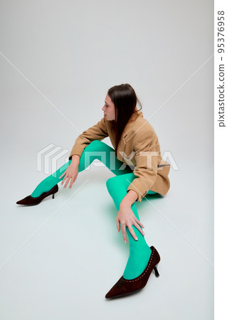 Portrait of young girl posing in green tights, oversized jacket and heels isolated over grey studio background. Stylish look. Portrait of young girl posing in green tights, oversized jacket and heels isolated over grey studio background. Stylish look. 95376958