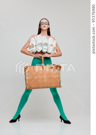 Portrait of young beautiful girl posing in green tights, paper bag and top made from slippers isolated on grey background. Unusual style Portrait of young beautiful girl posing in green tights, paper bag and top made from slippers isolated on grey background. Unusual style 95376980