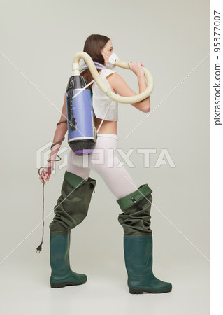 Portrait of young girl in rubber boots, vacuum cleaner on back and mask isolated on grey background 95377007