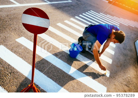 Road service worker paints striped pedestrian crossing on asphalt with paint brush. Markings for Road service worker paints striped pedestrian crossing on asphalt with paint brush. Markings for 95378289