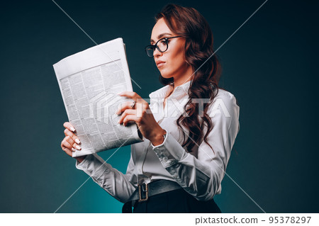 Beautiful young business woman in glasses holds newspaper in her hands and reads carefully. Study of Beautiful young business woman in glasses holds newspaper in her hands and reads carefully. Study of 95378297