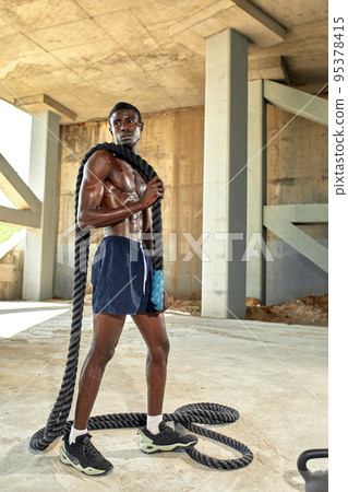 Rope workout. Sport man doing battle ropes exercise outdoor. Black male athlete exercising, doing functional fitness training with heavy rope Rope workout. Sport man doing battle ropes exercise outdoor. Black male athlete exercising, doing functional fitness training with heavy rope 95378415
