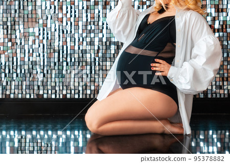 Elegant pregnant woman in a black bodysuit sitting on legs. Copy space. Close up. Shine beautiful background. The concept of pregnancy and female health 95378882