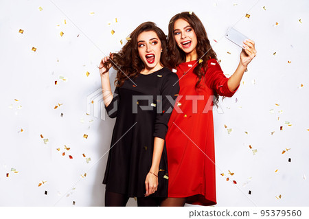 portrait of two happy young women who make selfie. in evening dresses on party over white background. 95379560