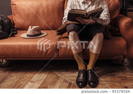 a man is reading a book at home on a leather sofa. vintage style orange brown color and shades. coziness and comfort leisure at home loft interior 95379584