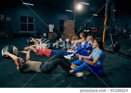Young men and women in sports uniform workout at sport gym, indoors. Sport, active lifestyle, health, youth concept Young men and women in sports uniform workout at sport gym, indoors. Sport, active lifestyle, health, youth concept 95380024