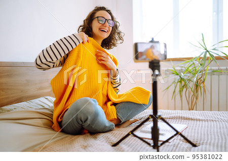 Fashion blogger. Young woman blogger talking with followers, live streaming and showing yellow sweater. 95381022