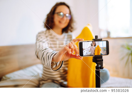 Fashion blogger. Young woman blogger talking with followers, live streaming and showing yellow sweater. Fashion blogger. Young woman blogger talking with followers, live streaming and showing yellow sweater. 95381026