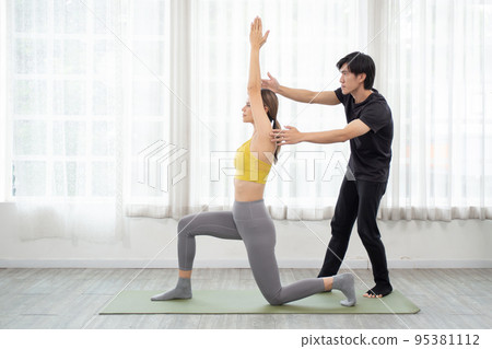 Young coach man training woman practicing yoga while stretching hands and balance in the room. Young coach man training woman practicing yoga while stretching hands and balance in the room. 95381112