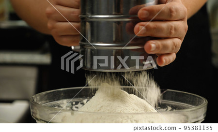 Close-up of a cook sifting flour through a metal sieve into a glass bowl. Side view. The concept of the bakery. Cake with his own hands. Close-up of a cook sifting flour through a metal sieve into a glass bowl. Side view. The concept of the bakery. Cake with his own hands. 95381135