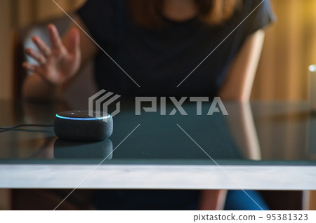 A woman talking to a smart speaker that recognizes voice while sitting in a chair A woman talking to a smart speaker that recognizes voice while sitting in a chair 95381323