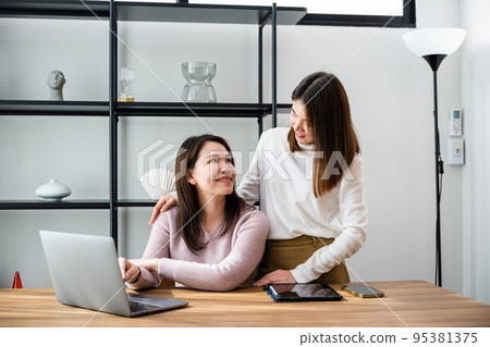 Asian mother and teenage daughter looking at laptop computer at home office 95381375