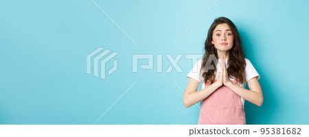 Please help me. Cute brunette woman asking for favour, holding hands in pray, begging you to buy something, standing against blue background Please help me. Cute brunette woman asking for favour, holding hands in pray, begging you to buy something, standing against blue background 95381682