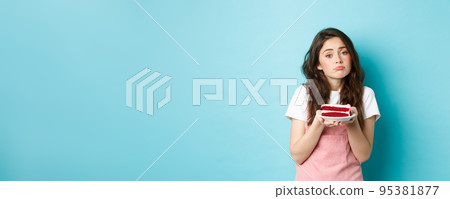 Holidays and celebration. Cute sad girl looking at camera upset, holding birthday cake with candle, feeling moody on b-day, standing over blue background Holidays and celebration. Cute sad girl looking at camera upset, holding birthday cake with candle, feeling moody on b-day, standing over blue background 95381877