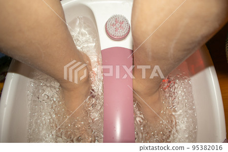 Close-up of feet in a tub with a vibrating foot massager. Electric foot massage bath and water bubbles. Pedicure and foot care Close-up of feet in a tub with a vibrating foot massager. Electric foot massage bath and water bubbles. Pedicure and foot care 95382016