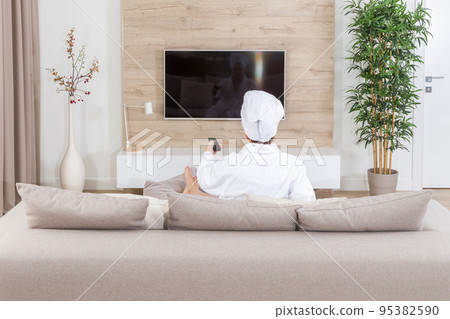 Woman sitting on a couch with towel on her head watching tv Woman sitting on a couch with towel on her head watching tv 95382590