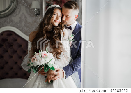 Beautiful young wedding couple posing with bouquet of flowers in hands Beautiful young wedding couple posing with bouquet of flowers in hands 95383952