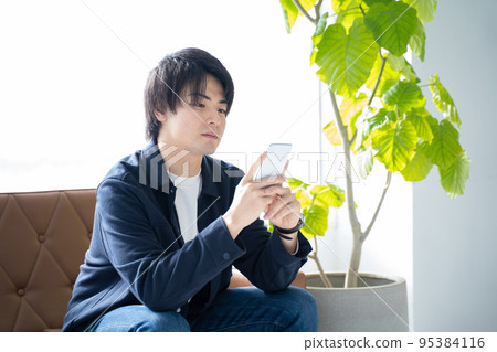 A man in his 20s who operates a smartphone-sit on the sofa in the living room and relax 95384116