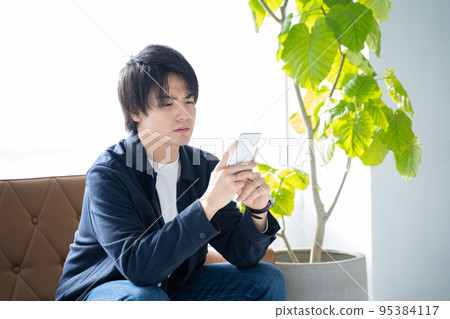 A man in his 20s who operates a smartphone-sit on the sofa in the living room and relax A man in his 20s who operates a smartphone-sit on the sofa in the living room and relax 95384117