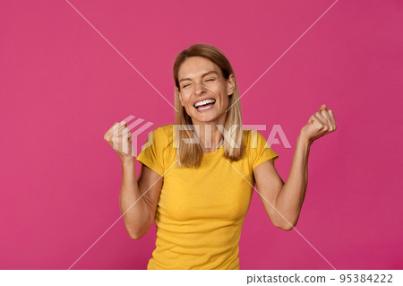 Cheerful adult european lady rejoices to victory and makes success gesture with hands Cheerful adult european lady rejoices to victory and makes success gesture with hands 95384222