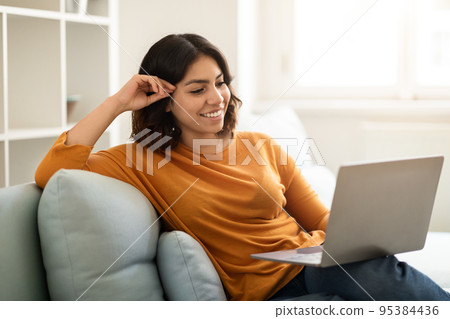 Smiling Young Arab Woman Relaxing With Laptop On Couch At Home Smiling Young Arab Woman Relaxing With Laptop On Couch At Home 95384436
