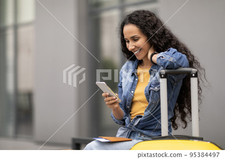 Happy lady travelling alone, using smartphone while waiting for boarding 95384497