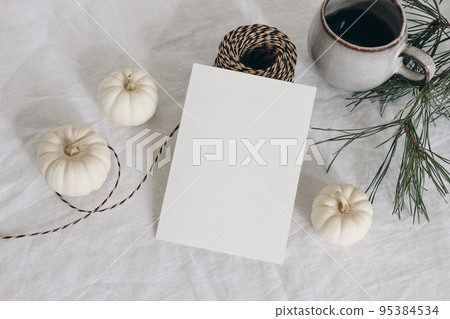Christmas stationery. Closeup of empty greeting card, invitation mockup. Cup of coffee, pine tree branches and decorative rope. Linen tablecloth. White pumpkins Winter, Thanksgiving flatlay, top view. 95384534