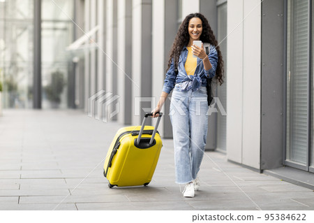 Cheerful middle eastern woman going vacation, walking by airport Cheerful middle eastern woman going vacation, walking by airport 95384622