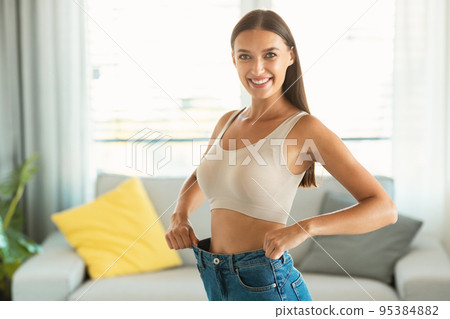 Slim Woman Wearing Old Oversized Jeans After Weight Loss Indoors 95384882
