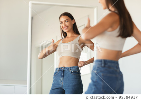 Happy Woman Gesturing Thumbs Up Approving New Size At Home Happy Woman Gesturing Thumbs Up Approving New Size At Home 95384917