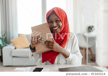 Satisfied african american muslim lady hugging cardboard box, getting online order parcel and smiling at camera 95385014