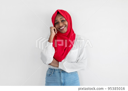 Smiling black muslim woman in hijab posing over white studio wall, looking at camera, free space. Muslim beauty concept Smiling black muslim woman in hijab posing over white studio wall, looking at camera, free space. Muslim beauty concept 95385016