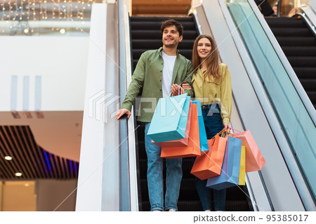 Couple Holding Bags Shopping Standing On Moving Stairs In Mall 95385017