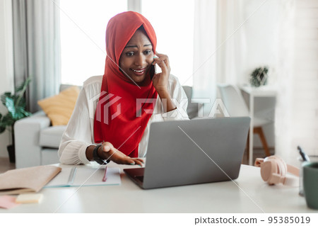 Problem concept. Frustrated black muslim woman talking on cellphone and using laptop, having problem 95385019