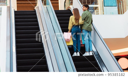 Buyers Couple Standing On Moving Stairs In Mall, Back View 95385182