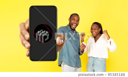 Joyful African Couple Showing Smartphone With Black Friday Offer, Studio Joyful African Couple Showing Smartphone With Black Friday Offer, Studio 95385188
