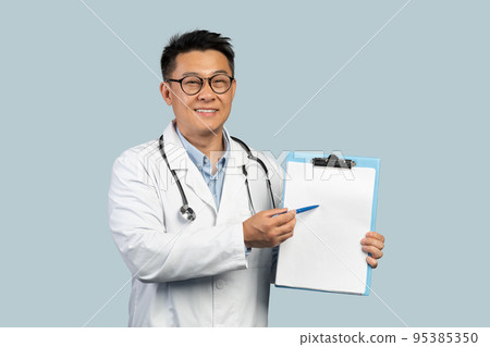 Smiling middle aged chinese male doctor in white coat and glasses shows on tablet with empty space Smiling middle aged chinese male doctor in white coat and glasses shows on tablet with empty space 95385350