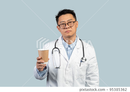 Tired unhappy middle aged chinese male doctor in white coat and glasses with cup of coffee takeaway 95385362