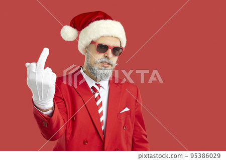 Bad Santa in red suit, hat and glasses shows middle finger and wishes you Merry Christmas 95386029